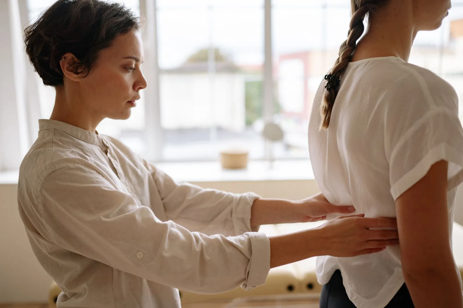Fisioterapeuta com as mãos na região lombar e pélvica de uma paciente deitada na maca