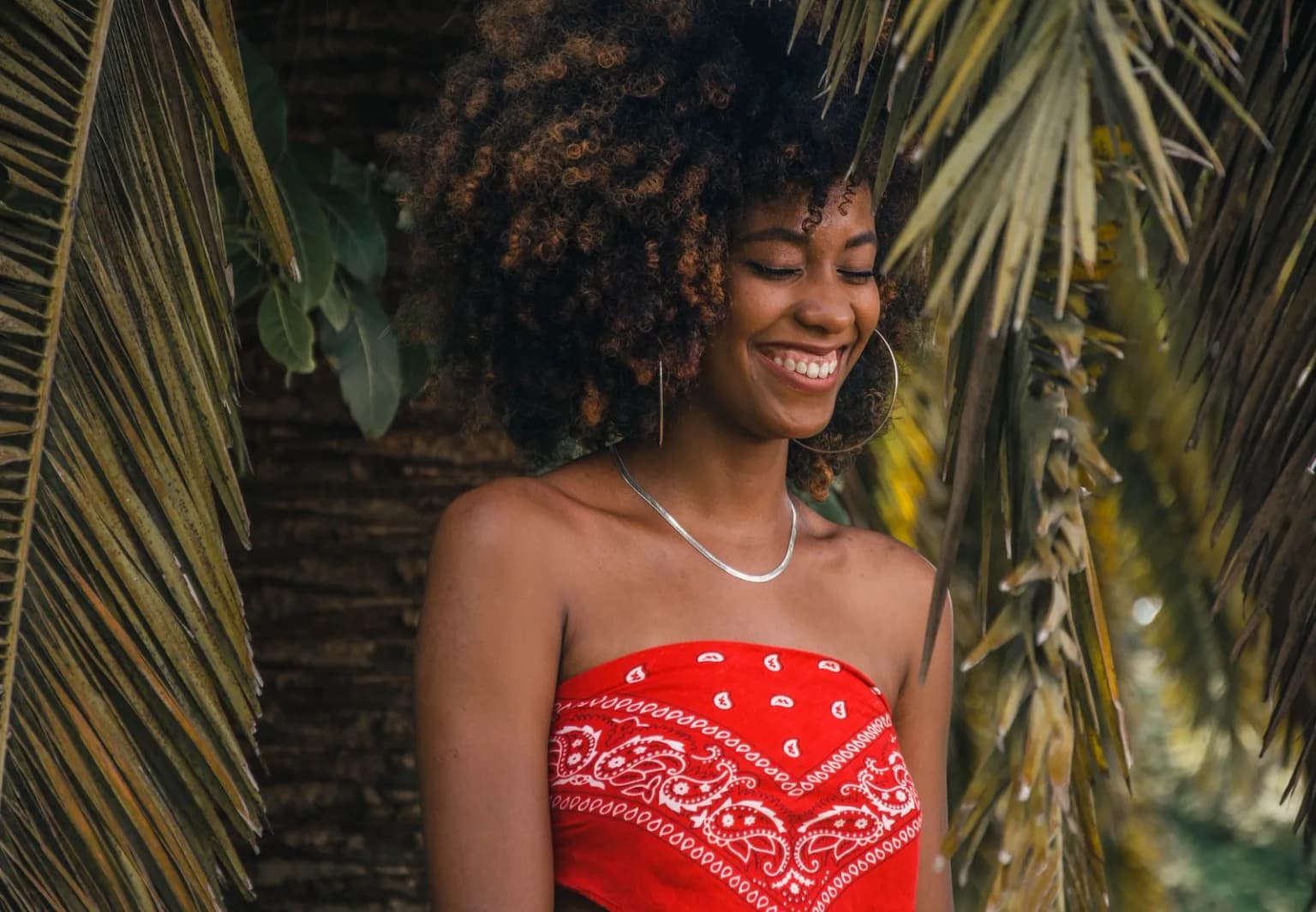Mulher jovem sorrindo sob folhas de palmeira, em luz natural